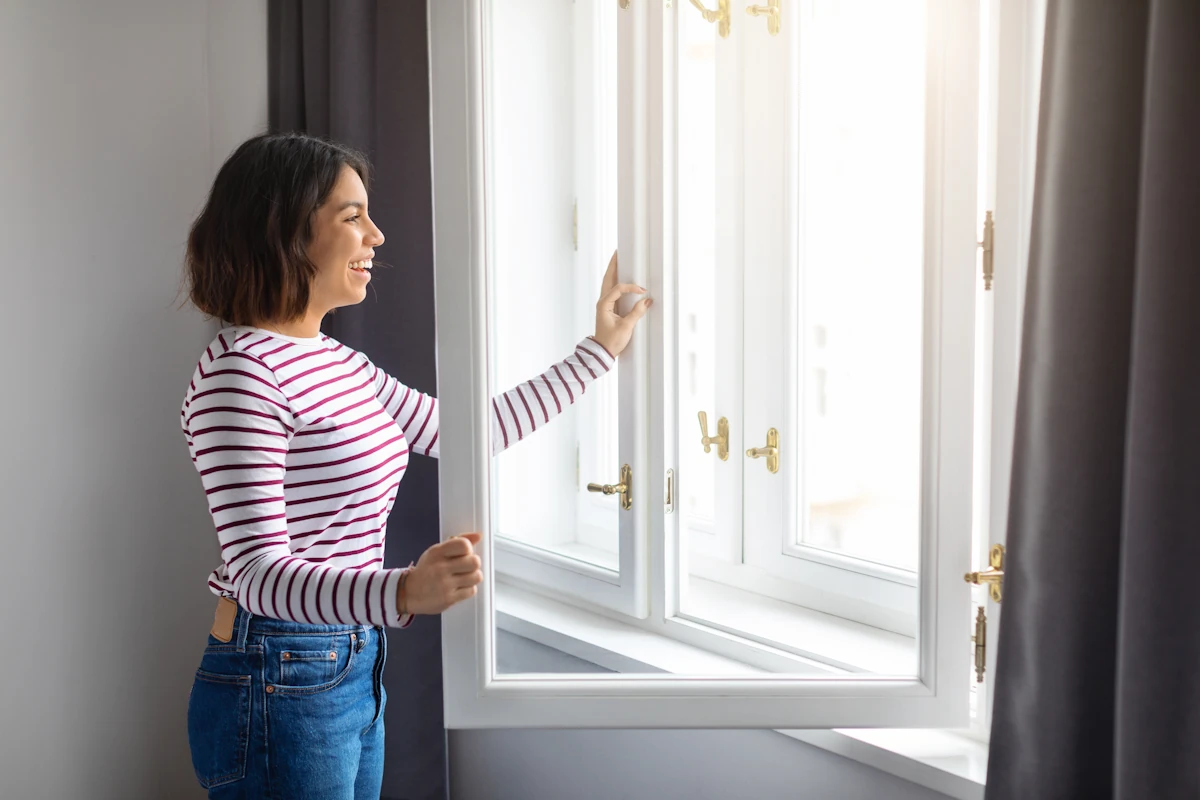 Une femme qui ouvre les fenêtres d'une maison