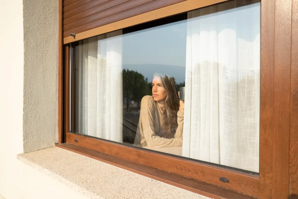 Une femme qui regarde par lune fenêtre en bois et alu